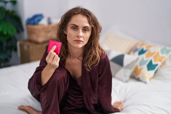 Beautiful Brunette Woman Holding Condom Bedroom Thinking Attitude Sober Expression — Stock Photo, Image