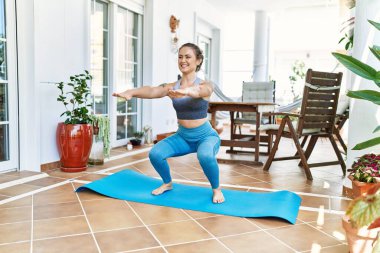 Güzel bir beyaz kadın evindeki terasta antrenman yapıyor ve esniyor. Asya 'da ve sağlıkta yoga minderinde çalışıyorum..