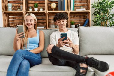 Evdeki kanepede oturan akıllı telefon kullanan genç çift..