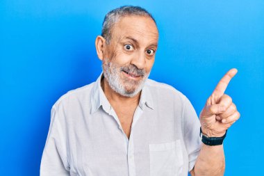 Sakallı, sıradan, beyaz tişörtlü, yüzünde kocaman bir gülümseme olan, eli ve parmağı kameraya bakan yakışıklı bir adam.. 