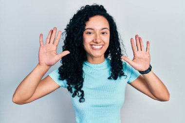 Young hispanic woman with curly hair wearing casual blue t shirt showing and pointing up with fingers number ten while smiling confident and happy. 