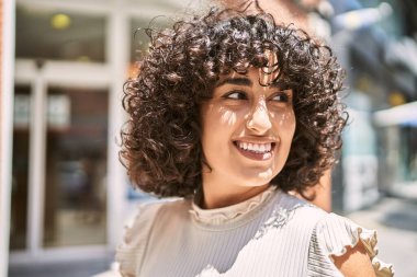 Orta Doğulu genç bir kadın gülümseyerek şehirde mutlu mesut dikiliyor..