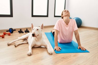 Genç beyaz kadın spor merkezinde köpekle esniyor.