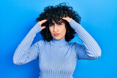 Orta Doğulu genç bir kadın. Elleri başının üstünde, günlük kıyafetler giyiyor. Stres yüzünden baş ağrısı çekiyor. migren ağrısı. 