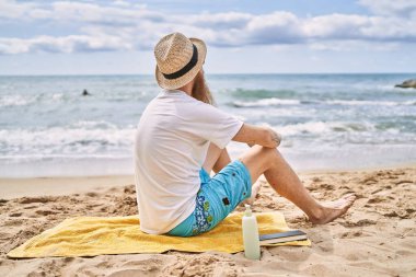 Genç kızıl saçlı turist plajda havlunun üzerinde oturuyor..