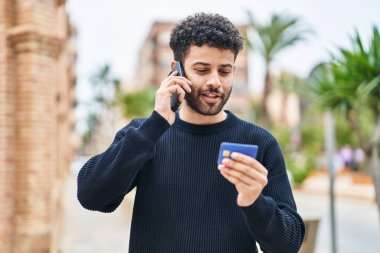 Sokakta akıllı telefon ve kredi kartı kullanan genç bir Arap.