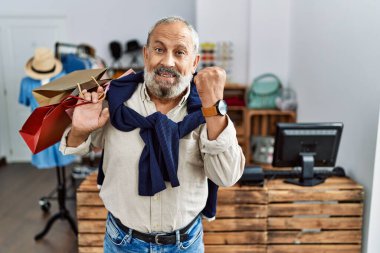Yakışıklı son sınıf öğrencisi butik dükkanında alışveriş torbaları tutuyor. Çok mutlu ve heyecanlı bir şekilde kollarını kaldırıp, gülümseyip başarı için bağırıyor. kutlama konsepti. 