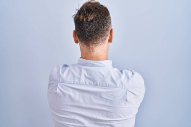 Middle age caucasian man standing over blue background standing backwards looking away with crossed arms 