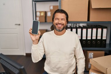 Küçük işletme şirketinde çalışan yakışıklı orta yaşlı bir adam elinde akıllı bir telefon tutuyor. Pozitif ve mutlu görünüyor. Dişlerini gösteren bir gülümsemeyle ayakta duruyor ve gülümsüyor. 