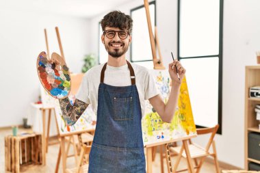 Genç İspanyol sanatçı gülümsüyor. Resim stüdyosunda fırça ve palet tutarken mutlu..