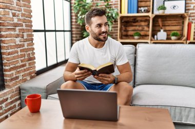 Genç İspanyol adam gülümsüyor evde kendinden emin bir şekilde kitap okuyor.