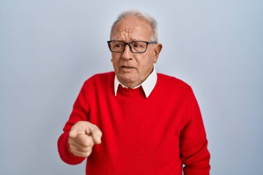 Gri saçlı yaşlı adam izole edilmiş arka planda dikiliyor. Kameraya kızgın ve sinirli olduğunu gösteriyor. 