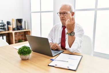 Senior man working at the office using computer laptop showing middle finger, impolite and rude fuck off expression 