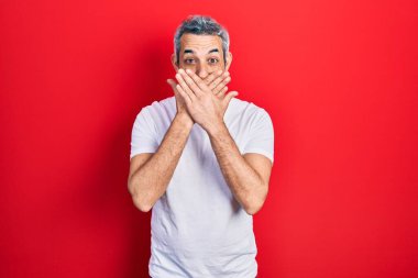 Gri saçlı, sıradan beyaz tişörtlü yakışıklı orta yaşlı bir adam ağzını yanlışlıkla ellerle kapatmış. gizli kavram. 