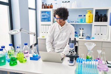 Laboratuvarda dizüstü bilgisayar kullanan Latin kökenli genç adam.