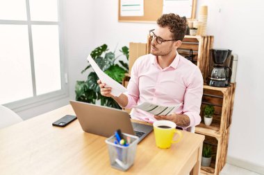 Ofiste çalışan Latin asıllı genç adam belgeleri okuyor.