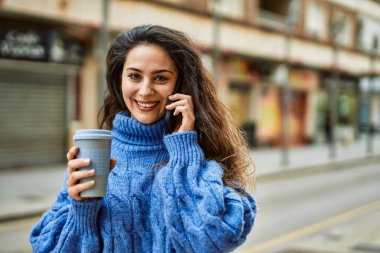 Genç İspanyol kadın akıllı telefondan konuşuyor ve şehirde kahve içiyor..