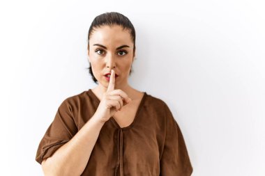 Genç esmer kadın izole edilmiş arka planda duruyor ve parmakları dudaklarında sessiz olmak istiyor. sessizlik ve gizli konsept. 