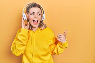 Güzel, beyaz bir kadın, kulaklık takıp müzik dinliyor. Başparmağıyla yan tarafa bakıyor ve ağzı açık gülümsüyor. 