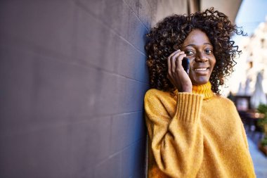 Afro-Amerikalı kadın gülümsüyor. Akıllı telefondan konuşuyor.