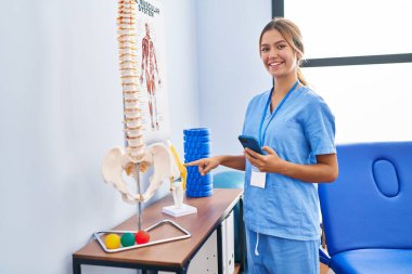 Genç İspanyol fizyoterapist. Rehabilitasyon kliniğinde akıllı telefon kullanarak gülümsüyor.