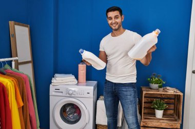 Çamaşır odasında deterjan şişesi tutan genç bir İspanyol.