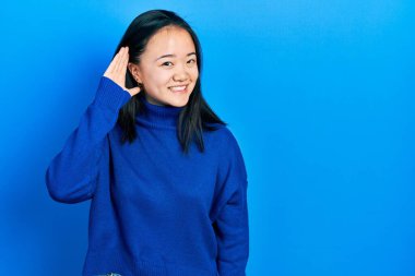 Günlük giysiler giymiş genç Çinli bir kız kulağından kulaklarına gülümseyerek dedikoduları ve dedikoduları dinliyor. Sağırlık kavramı. 