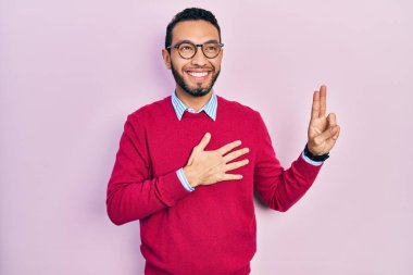 Sakallı, iş gömleği ve gözlüklü, gülümseyen, elleri göğsünde ve parmakları havada küfür eden, sadakat yemini eden İspanyol bir adam. 