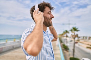 Genç İspanyol gülümseyen adam gezinti alanında müzik dinlemekten mutlu oluyor..