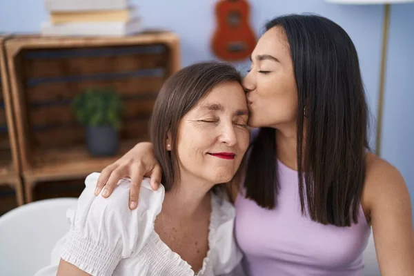 Two women mother and daughter sitting on table together kissing at home
