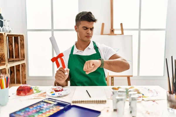 Young Hispanic Man Art Studio Holding Degree Checking Time Wrist — Stockfoto