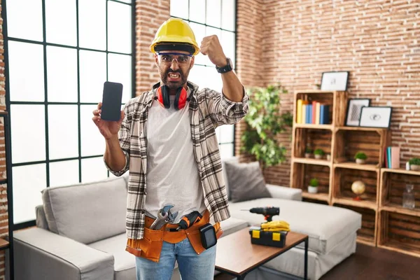 Young Hispanic Man Beard Working Home Renovation Holding Smartphone Annoyed — ストック写真