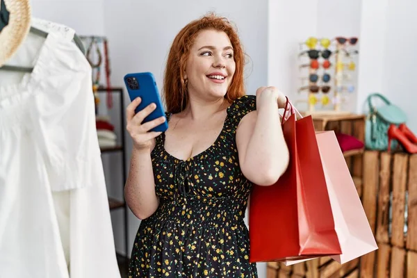 衣料品店でスマホショッピングをしている若い赤毛の女性 — ストック写真