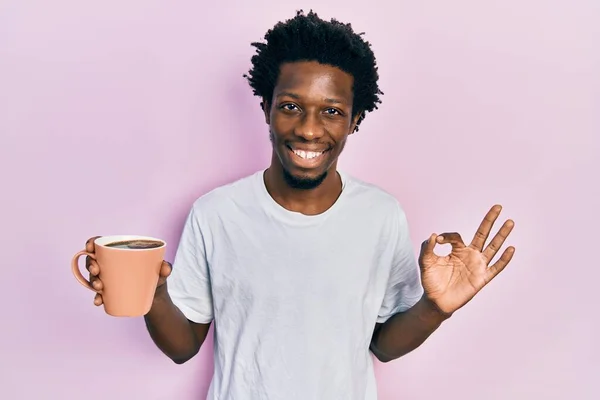 年轻的非洲裔美国人拿着一杯咖啡 手拿着手签 微笑着表示友善的手势 是极好的象征 — 图库照片