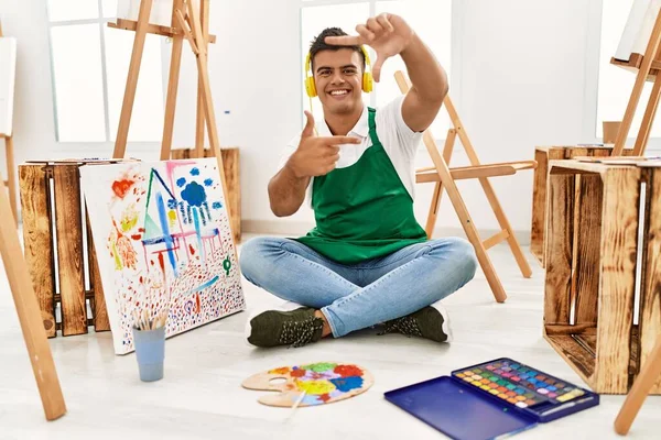 Young hispanic man at art studio smiling making frame with hands and fingers with happy face. creativity and photography concept.