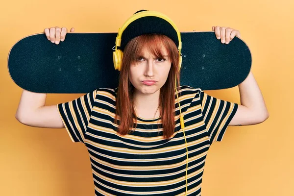 Redhead Young Woman Holding Skate Wearing Headphones Skeptic Nervous Frowning — Stock Photo, Image