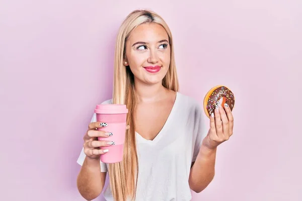 Jovem Loira Comendo Donut Bebendo Café Sorrindo Olhando Para Lado — Fotografia de Stock