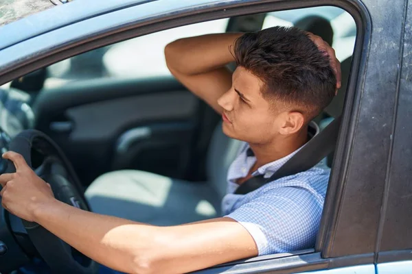 Young hispanic man unhappy driving car at street