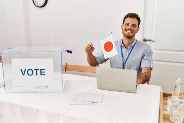 Joven Hispano Sonriendo Confiado Sosteniendo Bandera Japonesa Trabajando Colegio Electoral —  Fotos de Stock