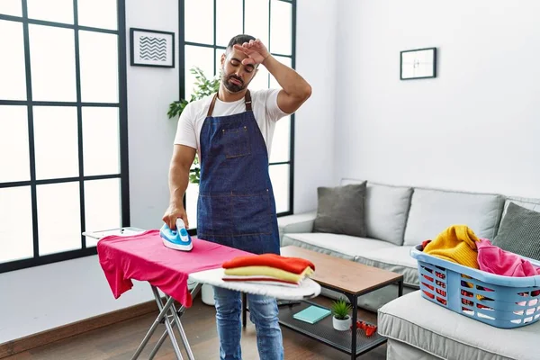 Young hispanic man unhappy ironing clothes at home