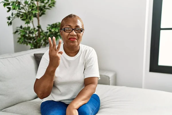 Mature Hispanic Woman Sitting Sofa Home Showing Pointing Fingers Number — Stock Fotó