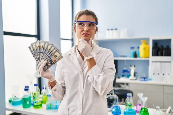 Young Woman Working Scientist Laboratory Holding Money Serious Face Thinking — Φωτογραφία Αρχείου