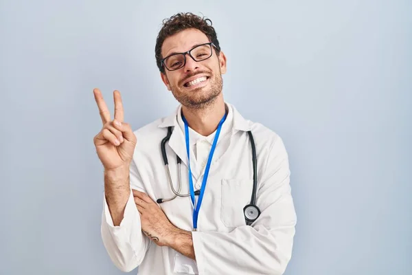 身穿医生制服的年轻人 戴着听诊器微笑着 喜形于色地在镜头前眨眼示意胜利 第二点 — 图库照片