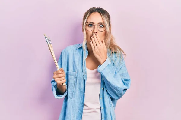 Beautiful Young Blonde Woman Holding Paintbrushes Covering Mouth Hand Shocked — Stock Fotó