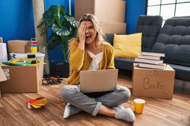 Young woman sitting on the floor at new home using laptop covering one eye with hand, confident smile on face and surprise emotion. 