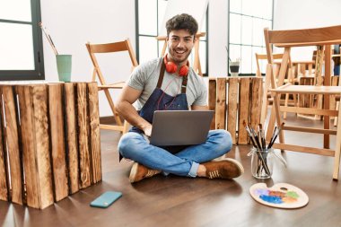 Sanat stüdyosunda kulaklık ve dizüstü bilgisayar kullanan İspanyol genç bir sanatçı..
