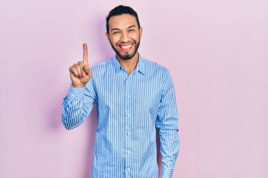 Sakallı, günlük mavi tişörtlü İspanyol bir numarayı gösterip işaret ederken kendinden emin ve mutlu bir şekilde gülümsüyor.. 