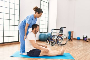 Orta yaşlı erkek ve kadın fizik tedavi kliniğinde rehabilitasyon seanslarına konsantre oluyorlar.