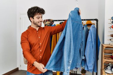 Genç İspanyol müşteri gülümsüyor. Giysi mağazasında tişörtlü bir askı tutuyor..