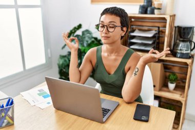 Ofiste yoga yaparken kendine gülen genç İspanyol kadın.